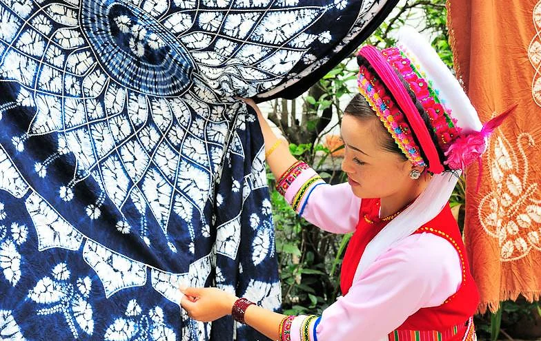 A Bai artisan presenting a detailed indigo tie-dyed textile near Dali