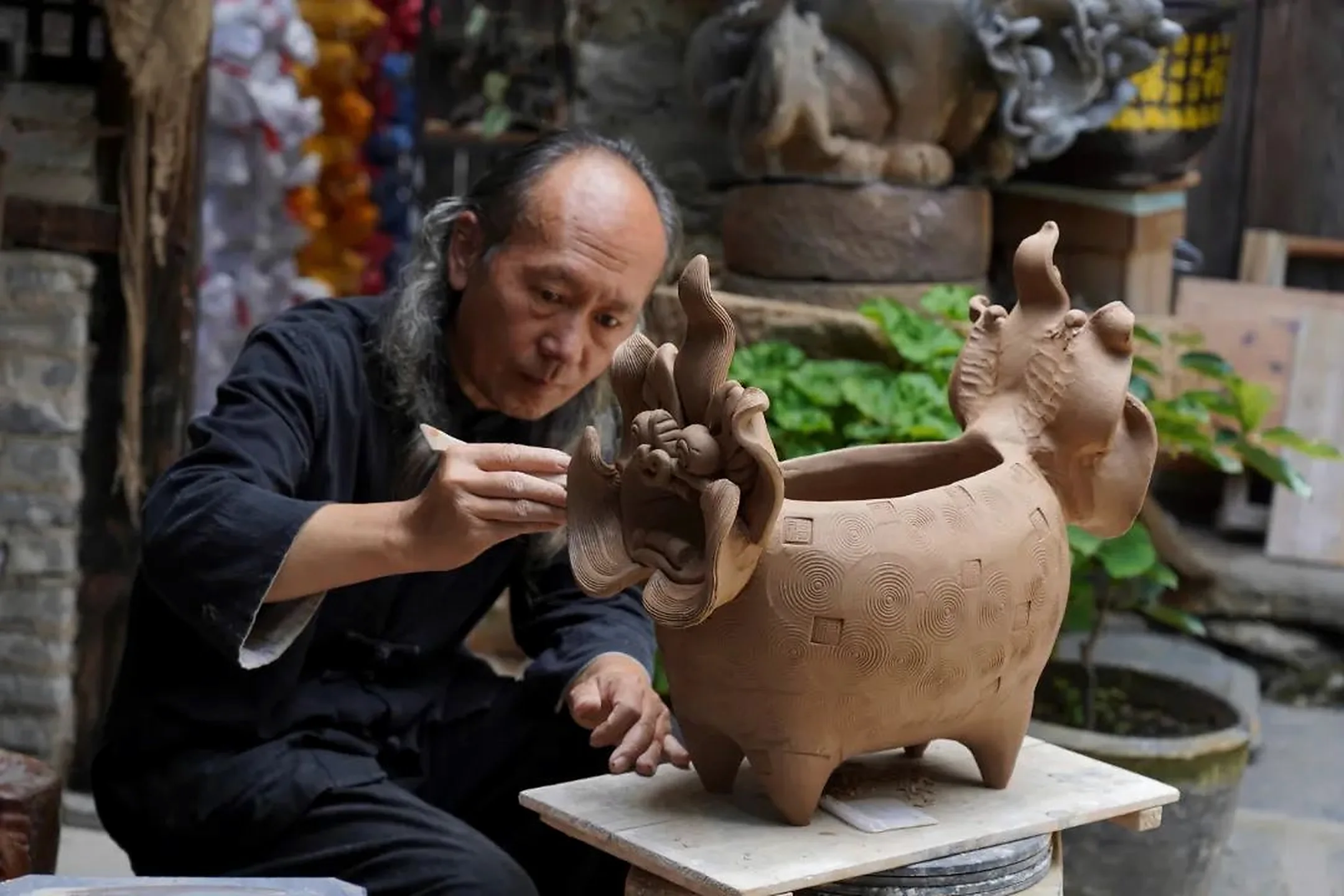 An artisan shaping a traditional tile cat sculpture in Dali